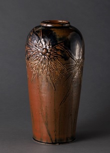 鉄釉花文花瓶 明治時代後期－1922年（大正11） 諏訪家蔵 底から肩部までわずかに開き、肩が張り、頸が短い花瓶にレリーフ状の花文があしらわれ、それにあわせて鉄釉の二重掛けで茶色と黒色の色彩表現を重ねている。花瓶の形状、レリーフの花文様、釉薬の使い方など、アール・ヌーボー様式に影響を受けた作品である。