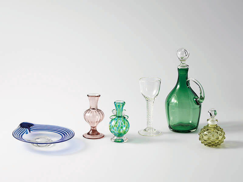 左から《線巻耳付皿》 1988-2012年、《 モールミニ花瓶 》1977-87年、《双耳ミニ花瓶》 1988-2012年、《エアーツイストワイングラス》 1977-87年、《手付デカンター 》 1977-87年、《 市松突起文栓付瓶 》1988-2012年