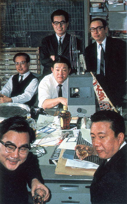 サン・アド草創期の面々 1967年（「ある会合 月曜日の企画会」『サンデー毎日』1967年4月30日号、p.67より。
前列左：開高健、右：矢口純。中列左：山崎隆夫、右：坂根進。後列左：柳原良平、右：山口瞳）